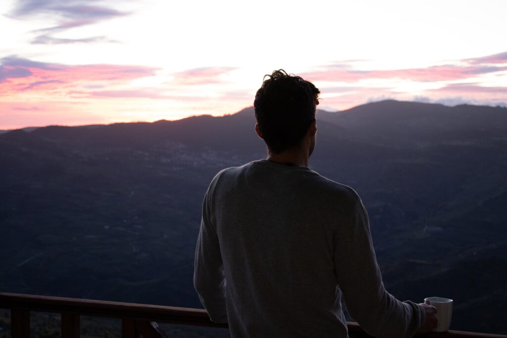 respiração profunda, a man standing on a balcony with a cup of coffee